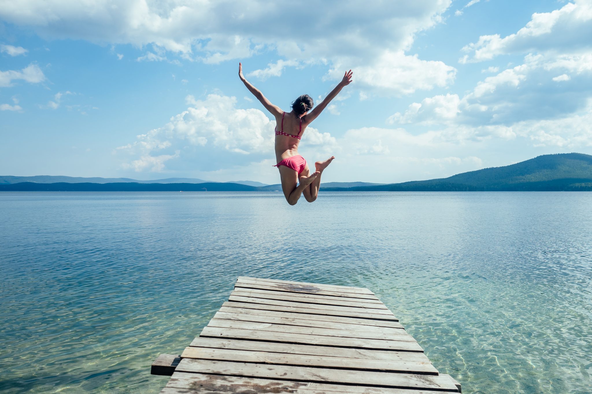 Die sommer. Девочка купальнике прыгает с пирса в воду.